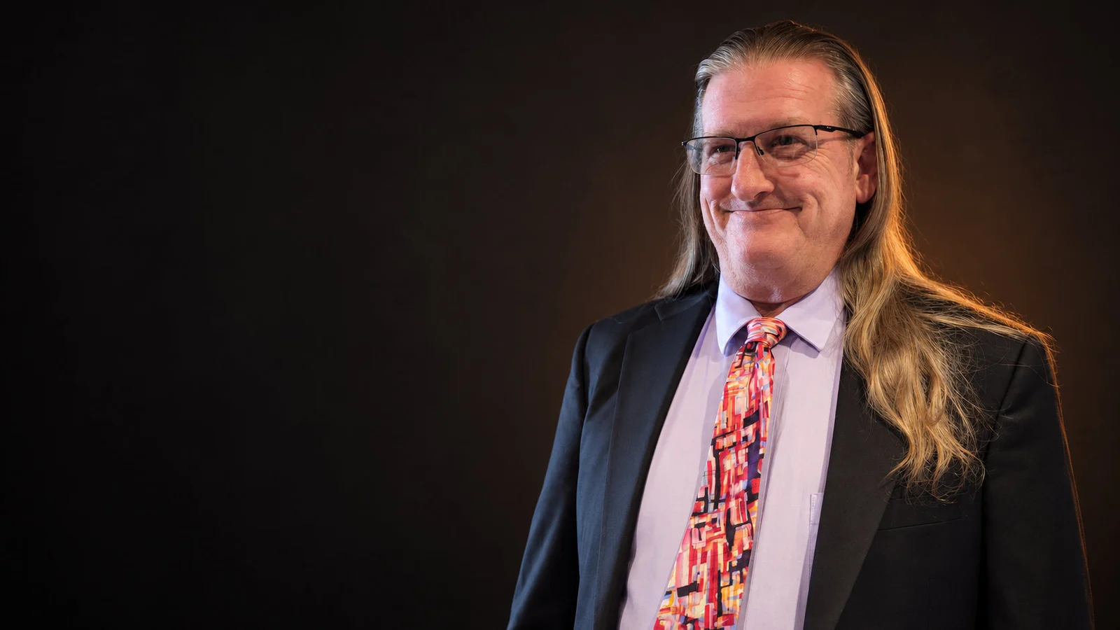 Ken Knorr in a dark suit against a charcoal background with warm copper lighting